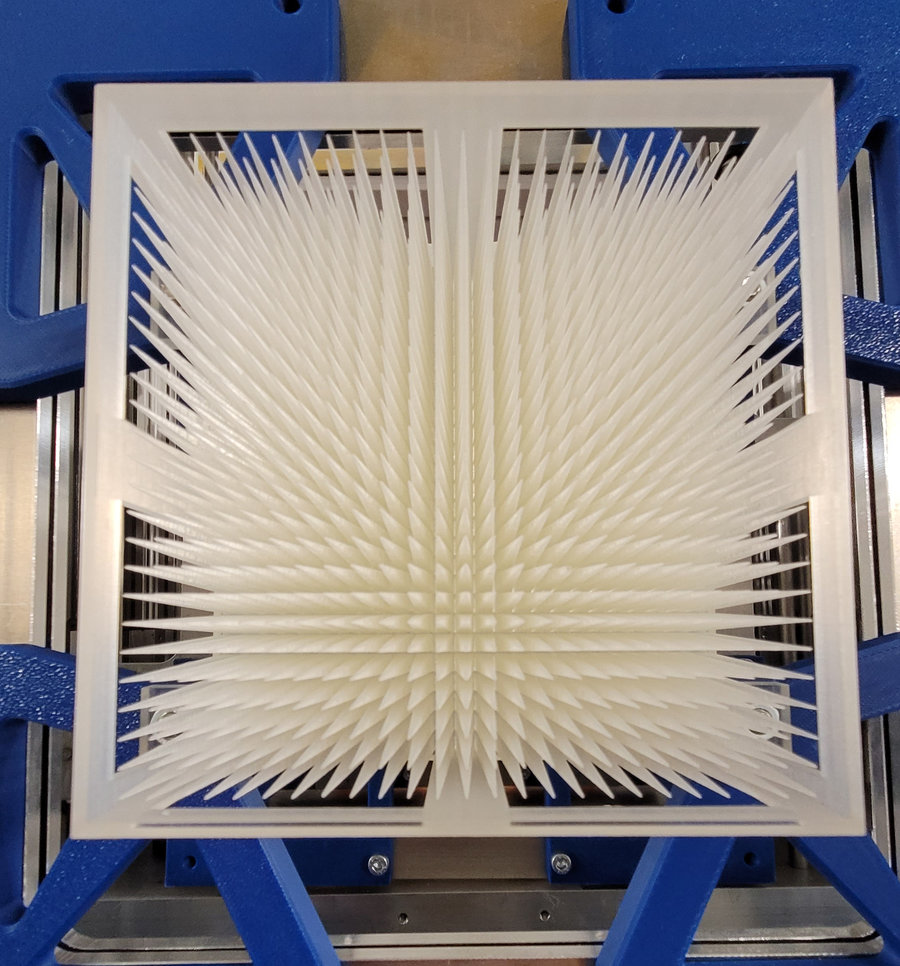 Modulator In einem blauen Metallrahmen ist ein weißes, rechteckiges Objekt mit vielen nach vorn ragenden Spitzen montiert.