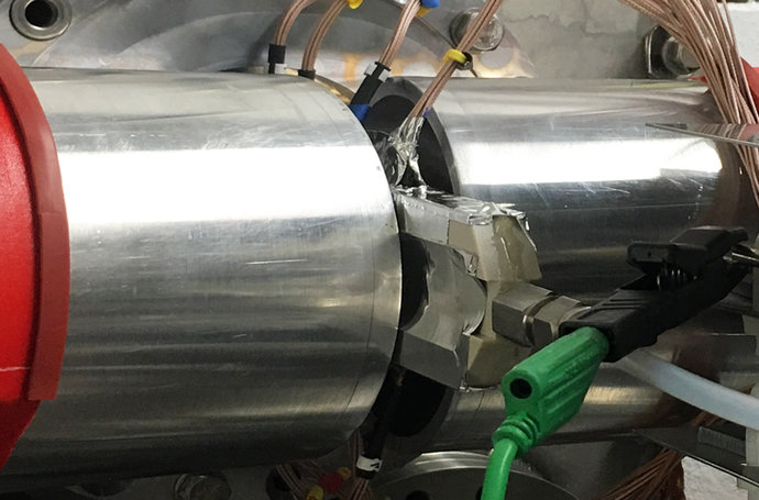 Eine mit Kabeln versehene Platte steckt in einem silbernen Zylinder. Eine mit Kabeln versehene Platte steckt in einem silbernen Zylinder.