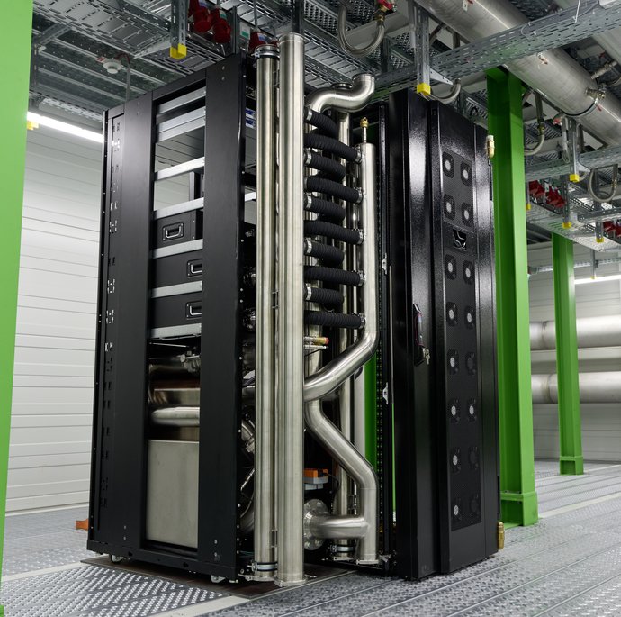 In einem industriellen Raum mit grünen Metallsäulen steht ein schwarzer Server mit silbernen Verrohrungen. In einem industriellen Raum mit grünen Metallsäulen steht ein schwarzer Server mit silbernen Verrohrungen.