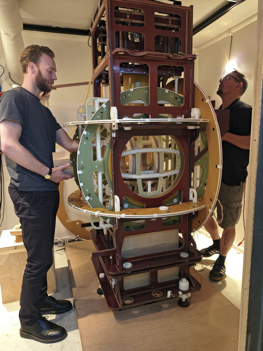 Experimentaufbau in Berlin Zwei Männer stehen rechts und links von einem überkopfhohen, verschachtelten Holzgerüst.