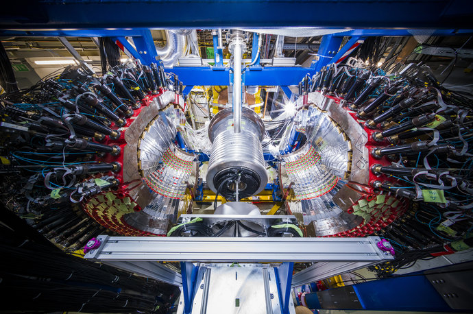 Two silver glittering half-spheres stand to the sides of a silver cylinder. Many cables lead away to the sides. Two silver glittering half-spheres stand to the sides of a silver cylinder. Many cables lead away to the sides.