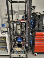 Experimentaufbau am Helmholt-Institut Mainz In einem Metallregal steht ein silberner Zylinder, darunter und darüber Messgeräte und Kabel.