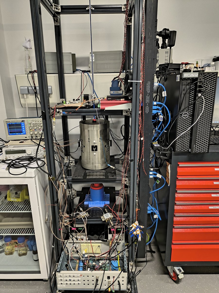 Experimentaufbau am Helmholt-Institut Mainz In einem Metallregal steht ein silberner Zylinder, darunter und darüber Messgeräte und Kabel.
